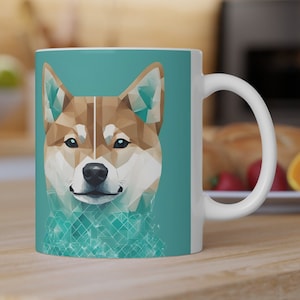 Könnte beinhalten: Weiße Keramiktasse mit tealfarbenem Hintergrund, auf dem eine geometrische Illustration eines Shiba Inu-Hundegesichts abgebildet ist.