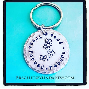 May include: Silver key chain with a round charm that says "Transformed for the better. Reborn." with three butterfly designs.