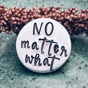 May include: A round silver charm with the words "NO matter what" written in black.