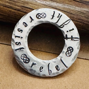 May include: A silver ring with the words "rebel" and "resist" engraved around the band. The ring also features a symbol of infinity.