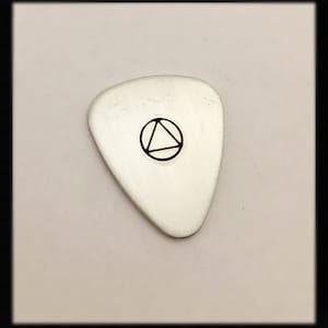 以下が含まれることがあります： 円の中に黒い三角形のデザインが施された銀色のギターピック