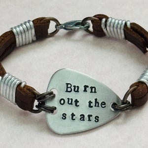 May include: Brown leather bracelet with silver metal accents and a silver metal guitar pick charm that says "Burn out the stars".