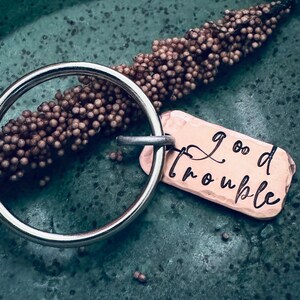 May include: A silver keyring with a copper tag that says "good trouble".