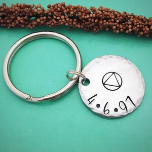 May include: Silver keychain with a round charm featuring a triangle symbol and the date 4.6.91.