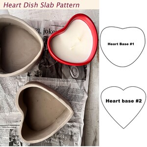 Puede incluir: Dos moldes de plato de cerámica en forma de corazón, uno de color marrón claro y el otro de color marrón oscuro. Los moldes están sobre un fondo de periódico. Hay un portavelas en forma de corazón rojo en el fondo.