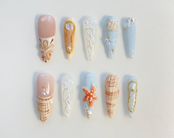 May include: Ten different nail designs featuring a beach theme. The designs include seashells, starfish, pearls, and flowers. The nails are painted in shades of blue, white, and pink.