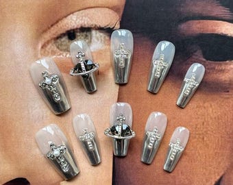 May include: Set of ten silver press-on nails with a white ombre effect. Each nail features a silver cross and a small, clear rhinestone. One nail has a black orb with a silver cross on top.