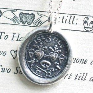 May include: Silver necklace with a round pendant featuring two intertwined hearts, a key, and the text "1525 MLS". The pendant is attached to a silver chain.