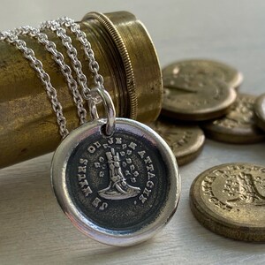 May include: A silver necklace with a round pendant featuring a boot design and the text "SECRETS OF THE JUNK ATTIC". The pendant is hanging from a silver chain and is surrounded by several gold-colored tokens.