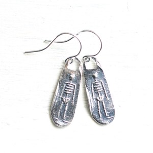 May include: Silver skeleton earrings with a textured finish. The earrings are shaped like a long oval and have a hook closure.