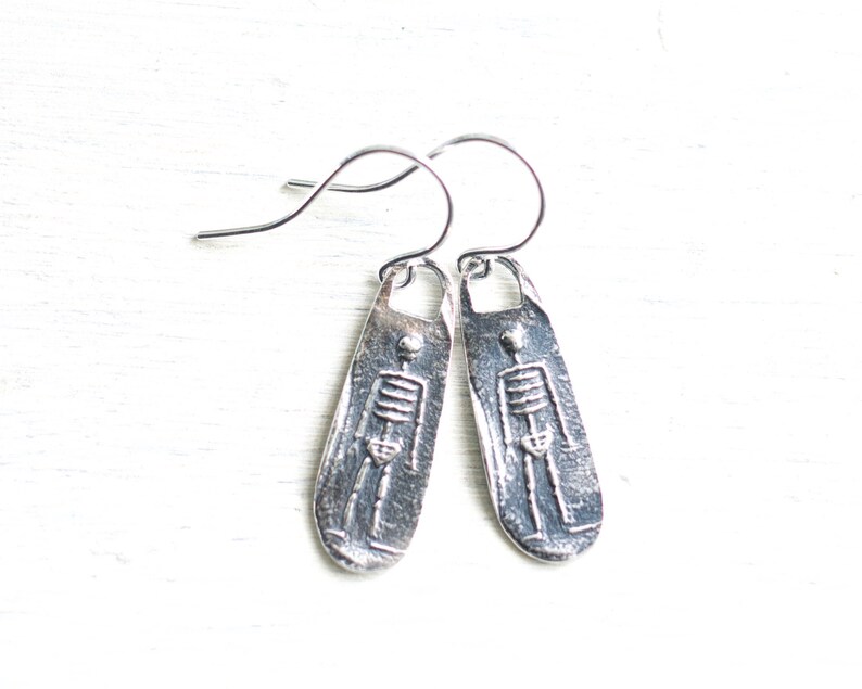 May include: Silver skeleton earrings with a textured finish. The earrings are shaped like a long oval and have a hook closure.