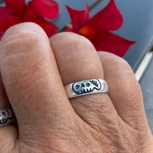 Pu&ograve; includere: Un anello d'argento con un designo a forma di teschio. L'anello &egrave; indossato su un dito.