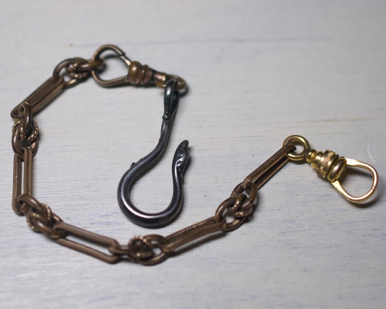 May include: A gold pocket watch chain with a black metal hook. The chain has a decorative design and a swivel clasp.