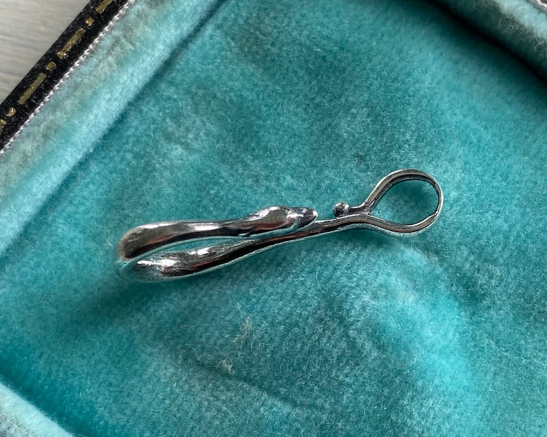 May include: A silver-toned metal clasp with a smooth, curved design. The clasp is open and appears to be a decorative element for a piece of jewelry.