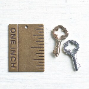 May include: A brass ruler with the words "ONE INCH" engraved on the side. The ruler is next to two antique-style keys, one gold and one silver.