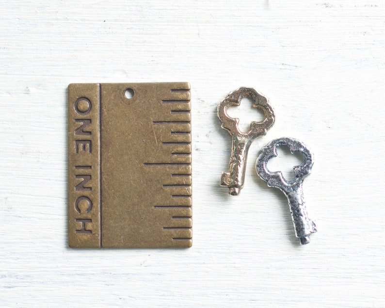 May include: A brass ruler with the words "ONE INCH" engraved on the side. The ruler is next to two antique-style keys, one gold and one silver.