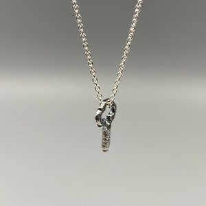 May include: A silver chain necklace with a small, textured silver pendant in the shape of a key.