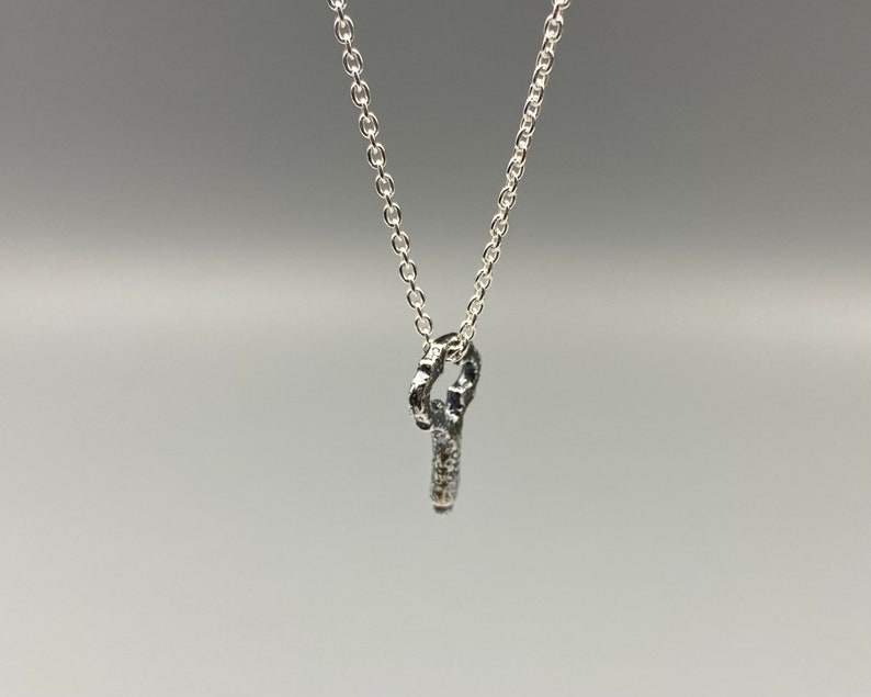 May include: A silver chain necklace with a small, textured silver pendant in the shape of a key.