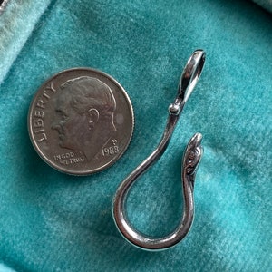May include: A silver-toned metal hook with a decorative snake head detail. The hook is on a turquoise blue surface.