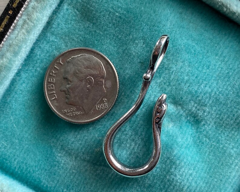 May include: A silver-toned metal hook with a decorative snake head detail. The hook is on a turquoise blue surface.