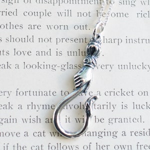May include: A silver necklace with a charm that is a hand holding a hook. The charm is detailed with a crown and other decorative elements.