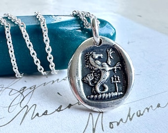 May include: Silver necklace with a silver pendant featuring a detailed depiction of a seahorse with a trident. The pendant is in the shape of a wax seal.