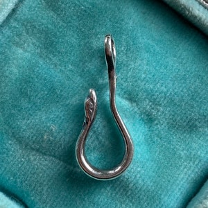 May include: A silver snake-shaped pendant charm with a smooth, polished finish. The charm is in the shape of a snake with its head curled around its body, forming a loop.