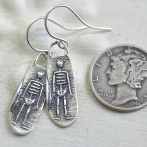 May include: A pair of silver skeleton earrings with a textured finish. The earrings are about the size of a US quarter.