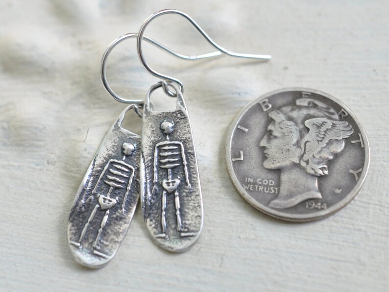 May include: A pair of silver skeleton earrings with a textured finish. The earrings are about the size of a US quarter.