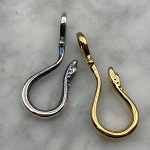 May include: Two silver and gold snake-shaped charms with a loop at the top. The charms are on a white marble surface.
