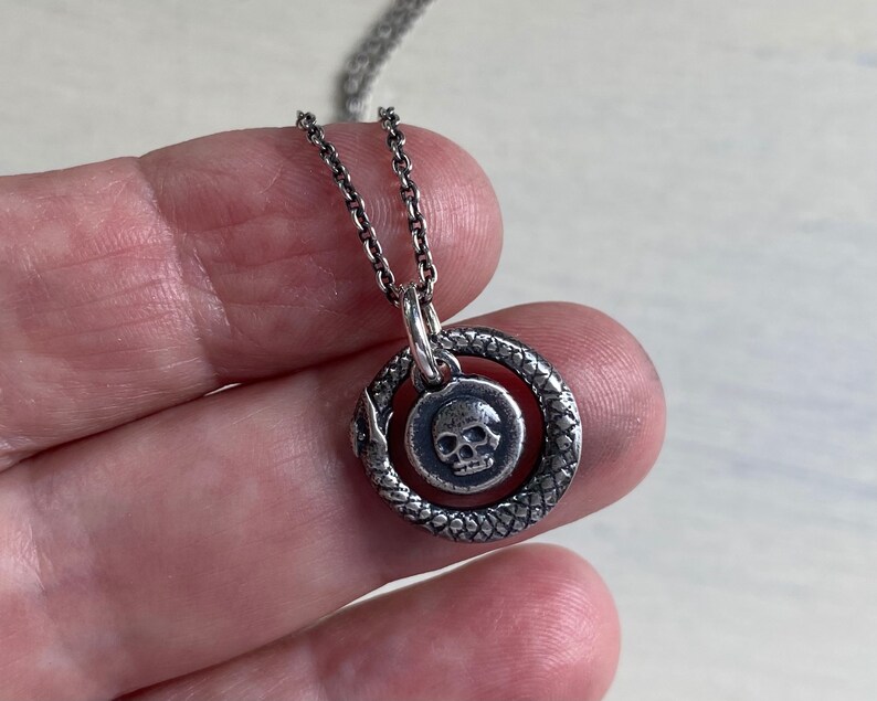 May include: A silver chain necklace with a pendant featuring a skull inside a circle with a snake-like design.