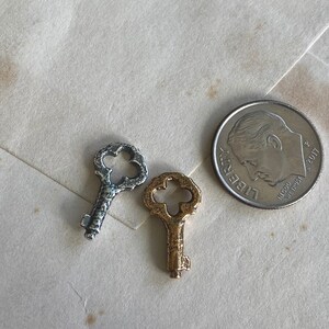 May include: Three antique-style keys, one silver and two gold, with intricate designs on the bow and bit. The keys are arranged on a white surface.