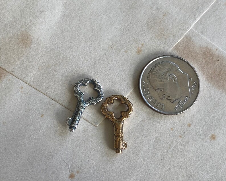 May include: Three antique-style keys, one silver and two gold, with intricate designs on the bow and bit. The keys are arranged on a white surface.