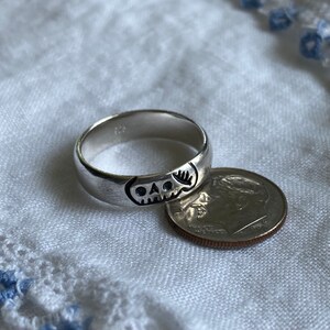 Pu&ograve; includere: Un anello d'argento con un designo a forma di teschio. L'anello &egrave; accanto a una moneta da dieci centesimi di dollaro americano per il confronto delle dimensioni.