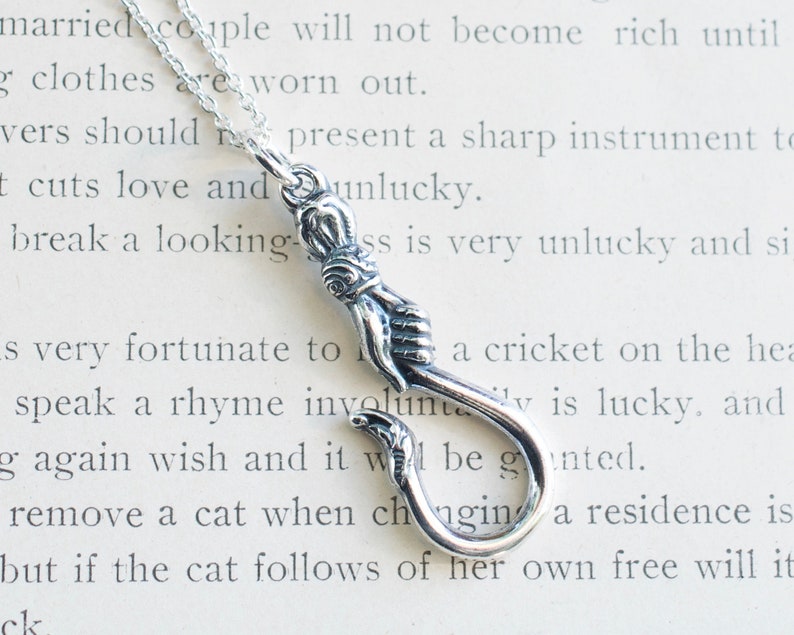 May include: A silver charm necklace with a hook and two hands clasped together. The charm is on a silver chain.