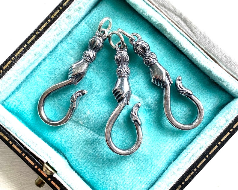 May include: Three silver hooks with a hand design. The hooks are in a blue velvet box.