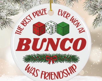 May include: White ceramic round ornament with gold string. The ornament features the text "THE BEST PRIZE EVER WON AT BUNCO WAS FRIENDSHIP" in red and green. Three dice with Christmas tree and dot designs are at the top.