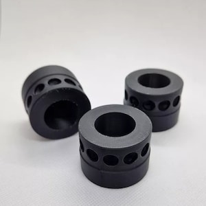Könnte beinhalten: Drei schwarze Gummringe mit einer Reihe kleiner Löcher am Außenrand. Die Ringe sind als Abstandshalter oder Stoßdämpfer konzipiert.