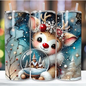 May include: A white tumbler with a colorful design of a reindeer holding a snow globe. The reindeer is wearing a red and green Christmas hat and has a red nose. The snow globe is filled with a winter scene and has a white church in the center. The background is a blue and white watercolor design with snowflakes and stars.