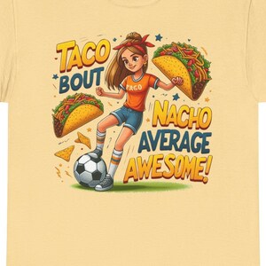 Peut inclure: Un t-shirt jaune avec une illustration de dessin animé d'une fille jouant au football avec des tacos et le texte "Taco Bout Nacho Average Awesome!"