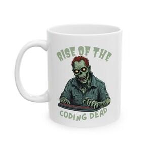 May include: White ceramic mug featuring a green zombie illustration with red hair and glowing yellow eyes, typing on a keyboard. The text "RISE OF THE" and "CODING DEAD" are printed in green.