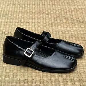 May include: A pair of black leather Mary Jane style shoes with a square toe and a strap that fastens with a silver buckle. The shoes are on a flat sole and appear to be new.