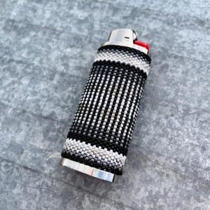 May include: A black and white beaded lighter cover with a silver metal base.