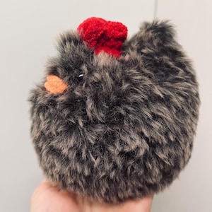 May include: A fluffy, round chicken toy with grey and brown fur. It has a bright red comb and an orange beak. The toy is designed to look like a fluffy chicken.