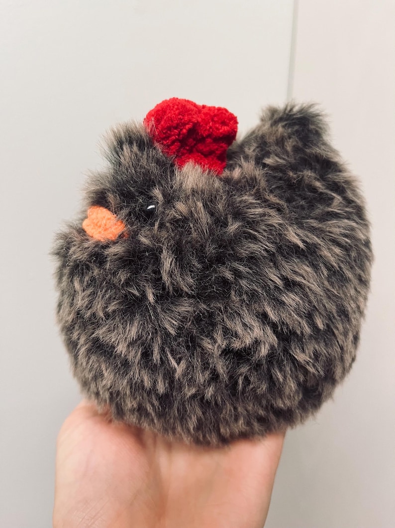 May include: A fluffy, round chicken toy with grey and brown fur. It has a bright red comb and an orange beak. The toy is designed to look like a fluffy chicken.