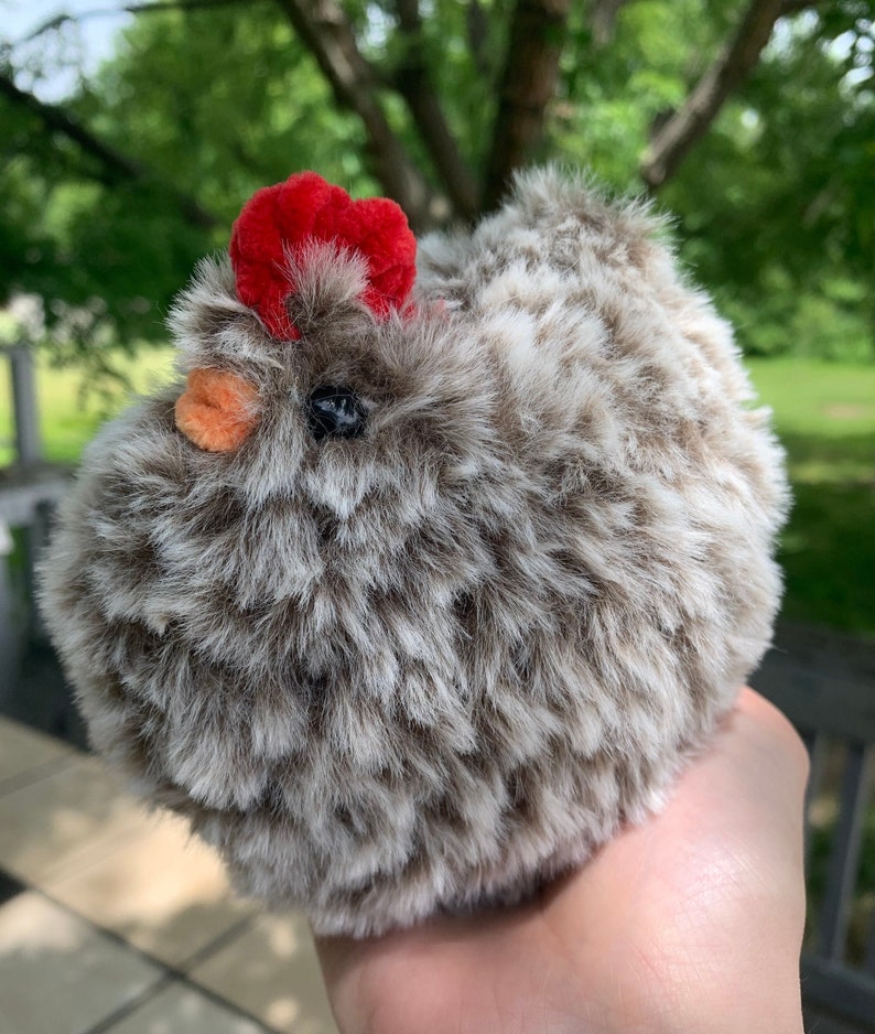 Fluffy chicken in brown and white fluffy yarn with red comb and orange beak in chenille yarn outside