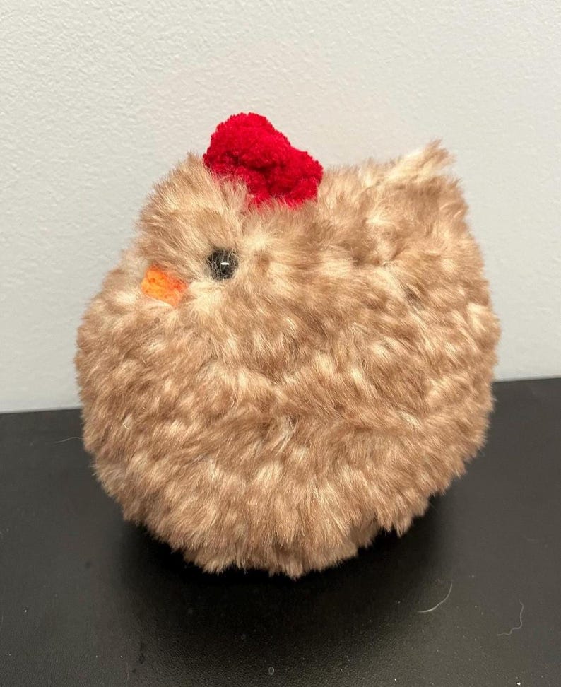 May include: A fluffy chicken toy with brown fur, a red comb, an orange beak, and a black eye. The stuffed animal is round and fluffy, resembling a chick. This soft toy is suitable for children.