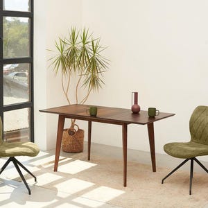 May include: A mid-century modern dining table with a dark wood finish, paired with olive green chairs. The table is set with two green mugs and a decorative vase. A woven basket and a potted plant add to the room's decor.