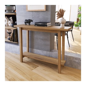 May include: A light brown wooden console table with a lower shelf. The table is rectangular and has four legs. A black rhino figurine and a book titled "The Fashion Book" are on the table. The table is 122 cm long.