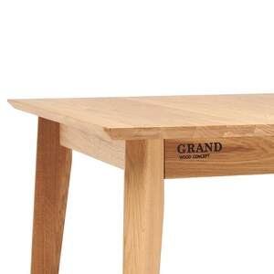 May include: A light-colored wooden table with a rectangular top and angled legs. The table has a natural wood grain finish. The words "GRAND WOOD CONCEPT" are printed on the side of the table.